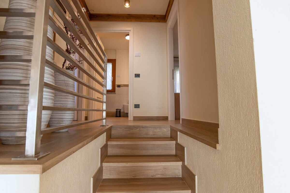 Una escalera con escalones de madera y barandilla metálica que lleva a un cuarto con pared blanca y una puerta.