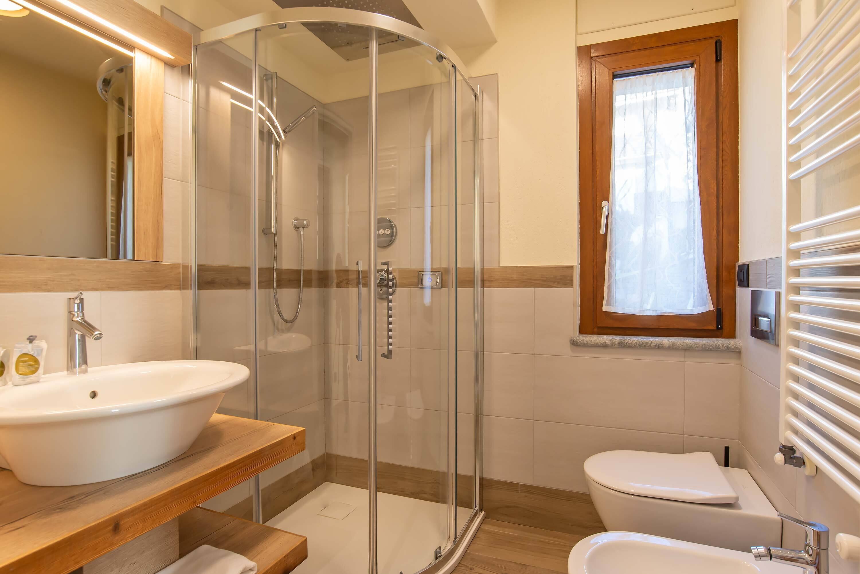 A modern bathroom with a glass-enclosed shower, a wooden vanity with a sink, a toilet, and a window with a wooden frame.