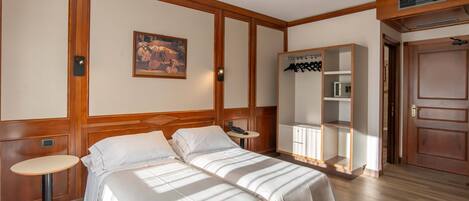 A hotel room with two beds, a small round table, a coat rack, and a wardrobe.