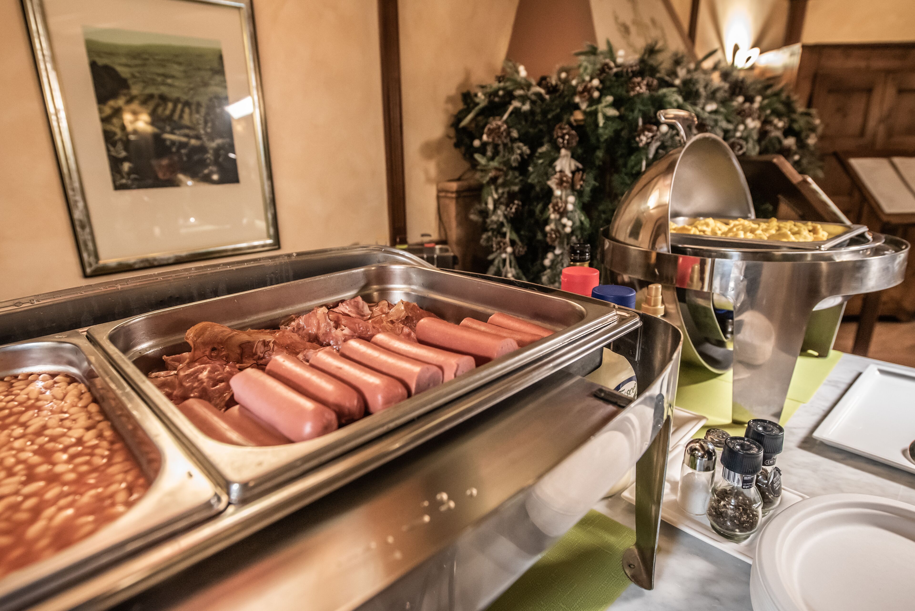 Un buffet proposant divers plats, notamment des hot-dogs, des haricots et un plat en sauce, qui contient probablement des pommes de terre ou un autre accompagnement riche en amidon.