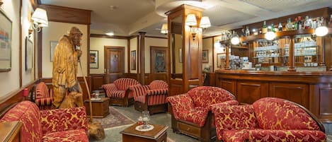 Un hall d’entrée traditionnel, avec des meubles en bois, une statue et un coin bar où sont exposées différentes bouteilles.