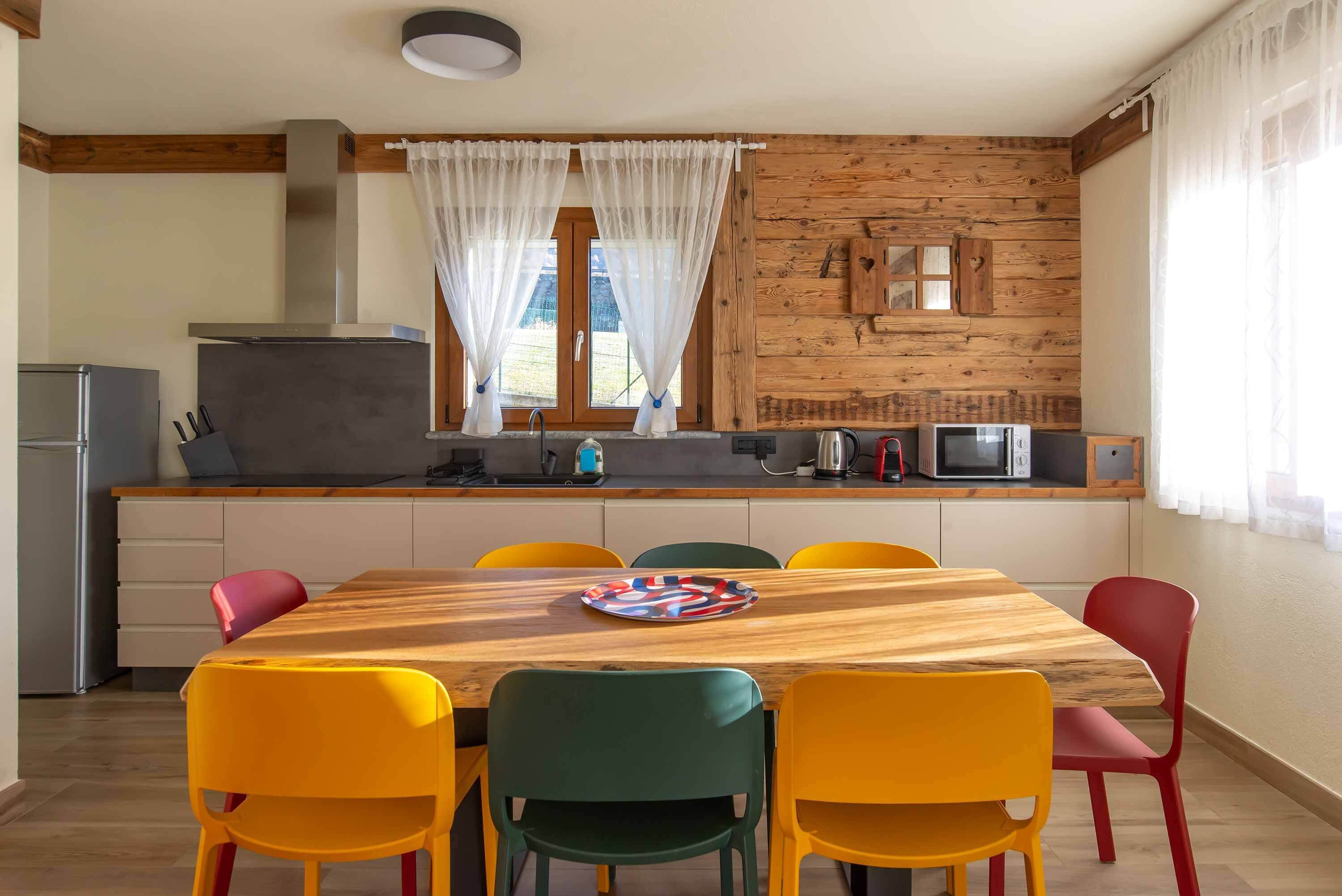 Una cocina con una mesa de madera y sillas coloridas, un refrigerador y un microondas.