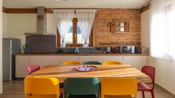 A kitchen with a wooden table and colorful chairs, a refrigerator, and a microwave.