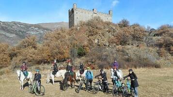 Un grupo de personas a caballo y en bicicleta frente a un castillo en una colina.
