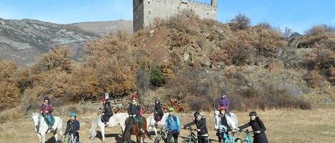 Un grupo de personas a caballo y en bicicleta frente a un castillo en una colina.