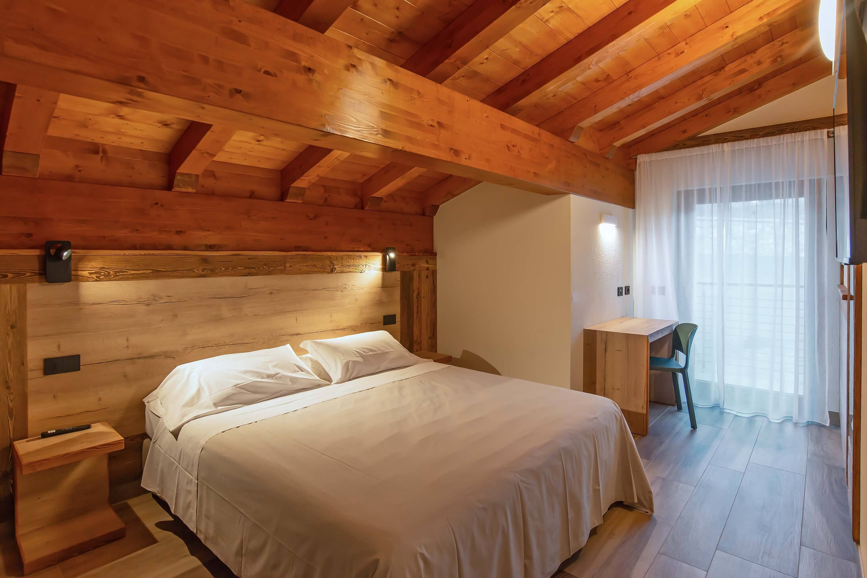 A wooden cabin bedroom with a bed, a desk, and a chair.