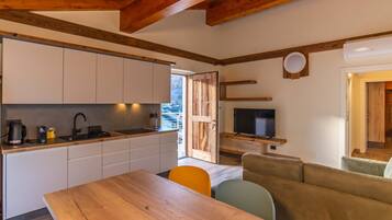 Una cocina moderna con armarios blancos, una mesa de comedor de madera y un televisor.