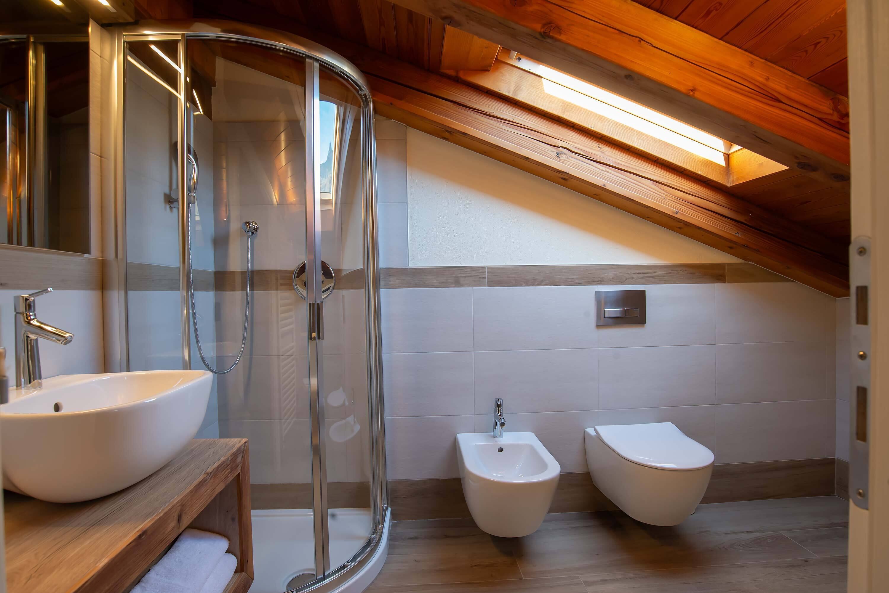 Un baño moderno con ducha de vidrio, tocador de madera con lavamanos y dos bidés.