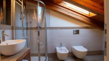 Un baño moderno con ducha de vidrio, tocador de madera con lavamanos y dos bidés.