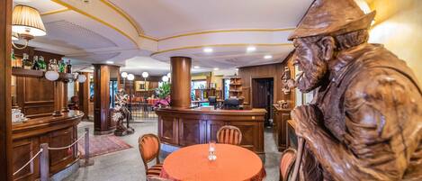 Uma área de bar com mobiliário de madeira, uma estátua e uma mesa redonda com cadeiras.