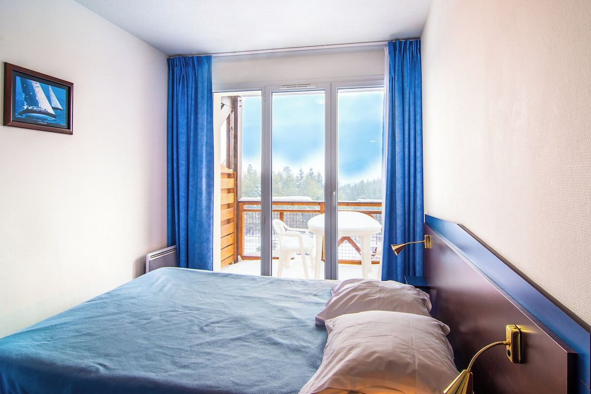 A hotel room with a bed, a view of a deck, and a framed picture on the wall.