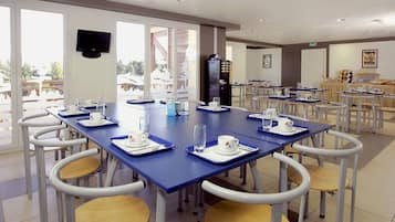Un espace repas avec des tables et des chaises, une machine à café et un téléviseur fixé au mur.