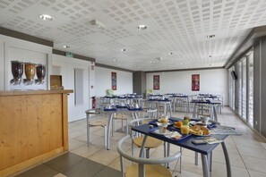 A cafeteria with tables and chairs, a wooden counter, and food items on trays.