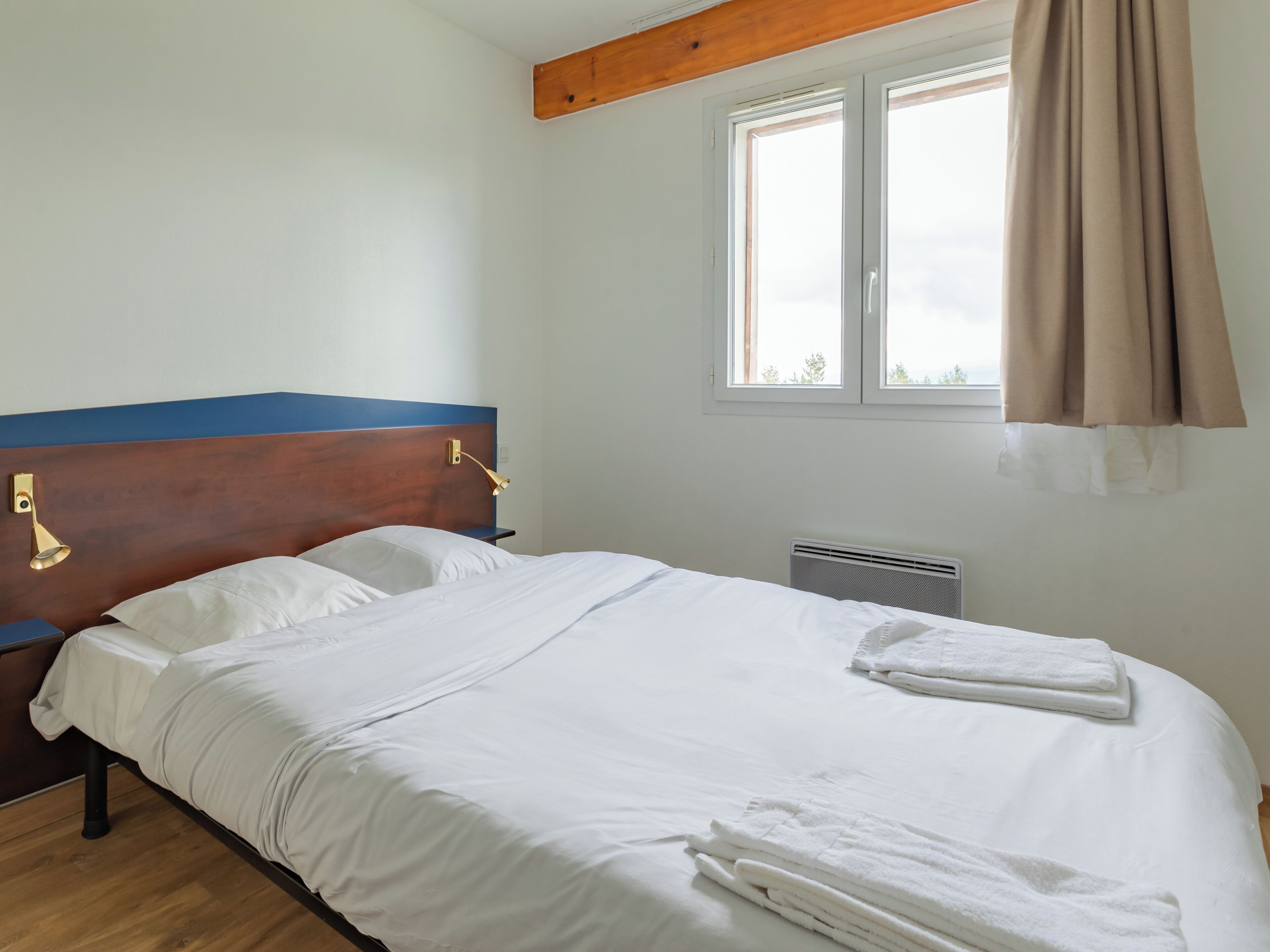 Una cama bien tendida con sábanas blancas, cabecera de madera y ventana con cortinas.