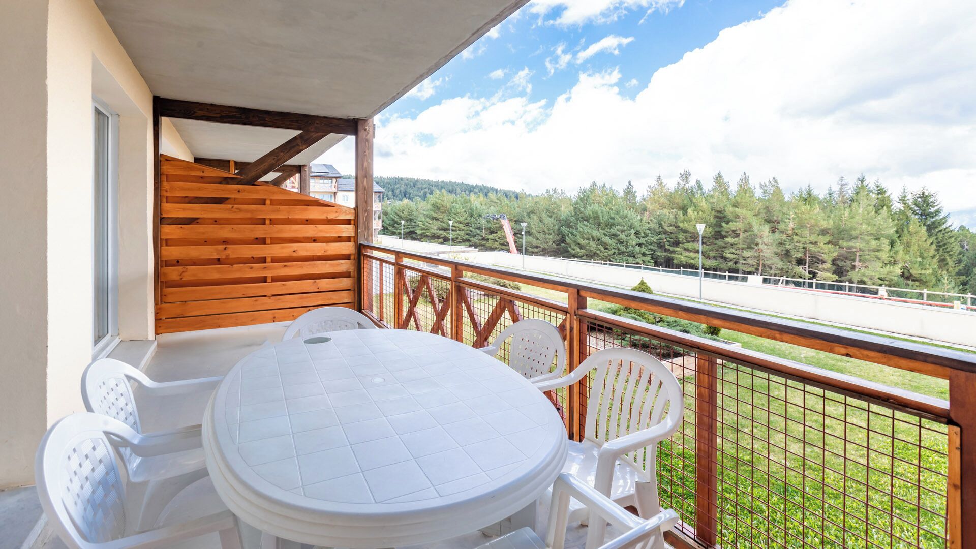 Un balcon avec une balustrade en bois, une table blanche et des chaises en plastique blanc.