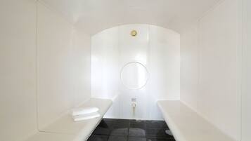 Una sala de sauna con dos bancos, un espejo circular y un letrero de advertencia.