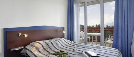 A hotel room with a large bed, a nightstand, a reading lamp, and a view of the outdoors through a sliding glass door.