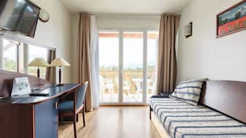 Camera d'albergo con un letto, una scrivania con una sedia, una televisione e una finestra con tende.