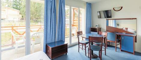 Habitación de hotel con cama, escritorio, silla, televisor y balcón con vistas al exterior.