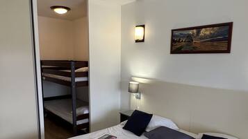 Una habitación de hotel con una litera, una cama individual, una lámpara fijada a la pared y un cuadro enmarcado.