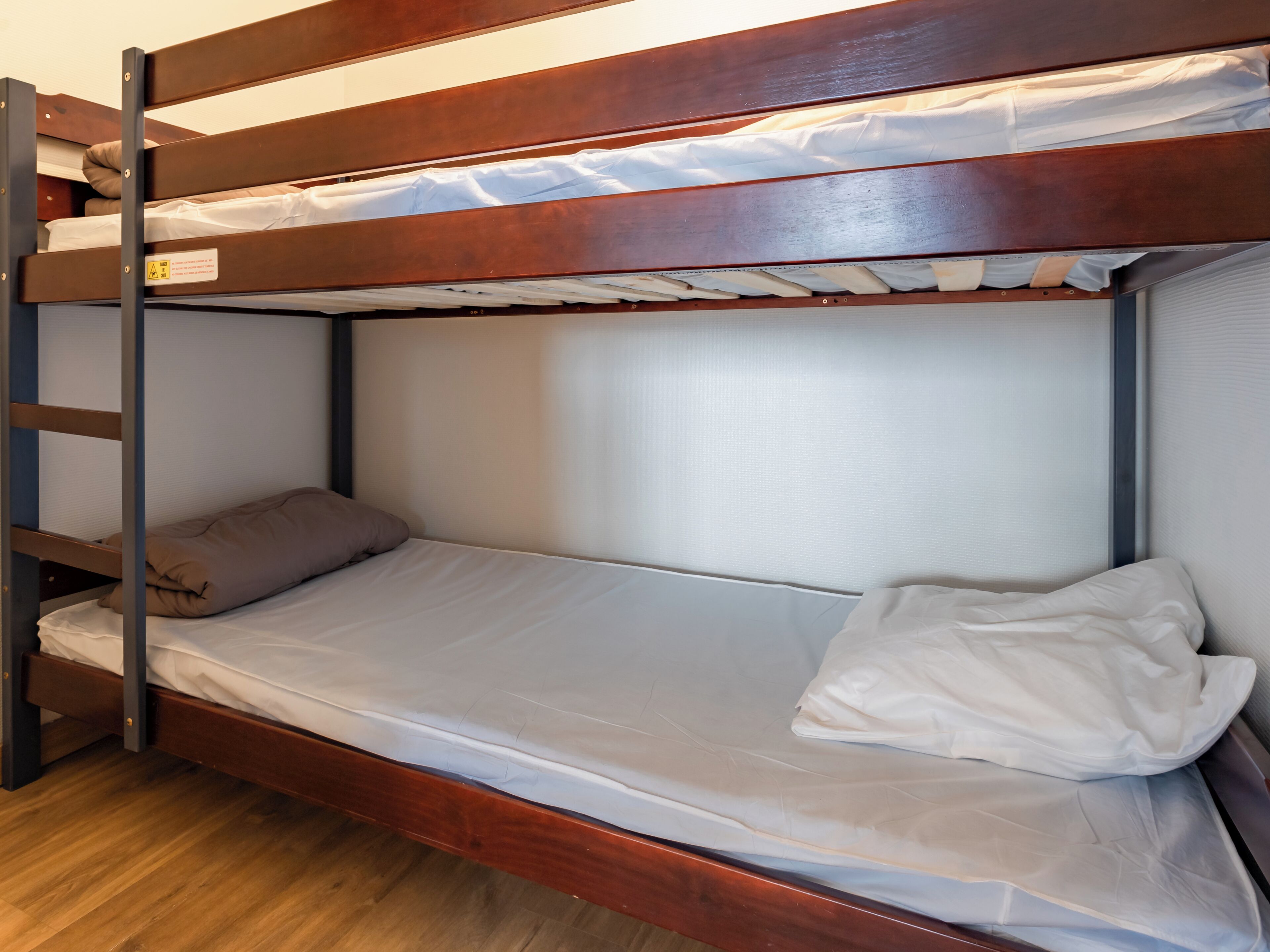 A bunk bed with a wooden frame, white bedding, and a pillow on the lower bunk.