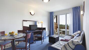 Une chambre d’hôtel comprenant un lit, un bureau avec un ordinateur, une chaise, une table à manger avec des chaises et une fenêtre avec des rideaux.