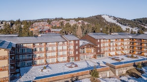 A multi-story hotel with balconies, a ski slope in the background, and a snowy ground.