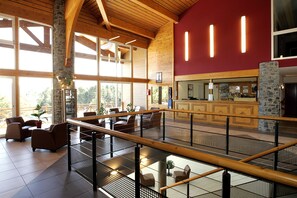 A spacious lobby with a wooden ceiling, stone pillars, and a glass railing overlooking a lower level. - Vacancéole - Appart Vacances Pyrénées 2000 (Bolquere)