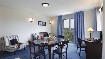 Una habitación de hotel con una mesa de comedor redonda, un sofá y un escritorio con una lámpara.