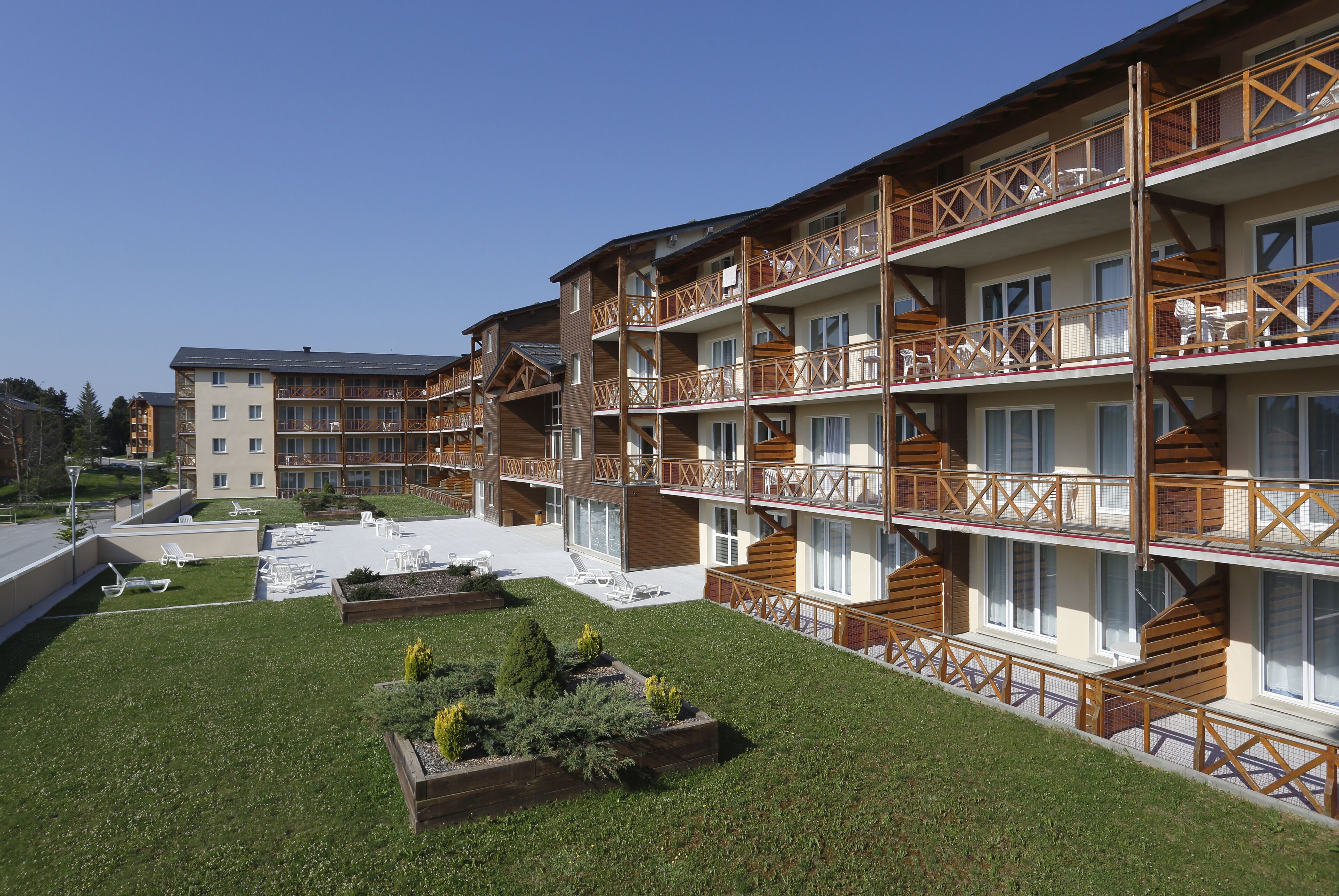 Ein mehrstöckiges Hotel mit Balkonen, einem Innenhof mit Sitzgelegenheiten im Freien und einem gepflegten Rasen.