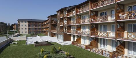 Ein mehrstöckiges Hotel mit Balkonen, einem Innenhof mit Sitzgelegenheiten im Freien und einem gepflegten Rasen.