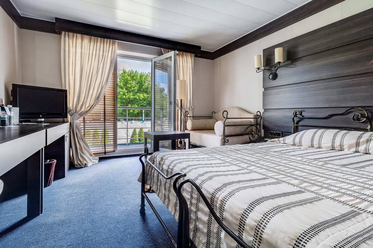 Une chambre d’hôtel moderne avec un grand lit, un bureau avec une télévision et un balcon avec des rideaux.