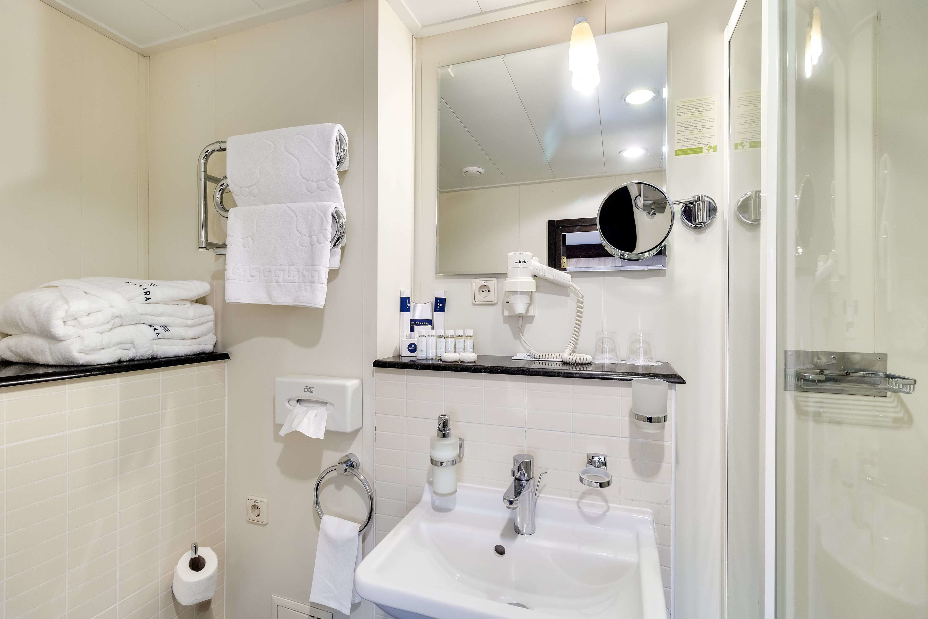 A modern bathroom with a white sink, two faucets, a mirror, and a glass shower enclosure.