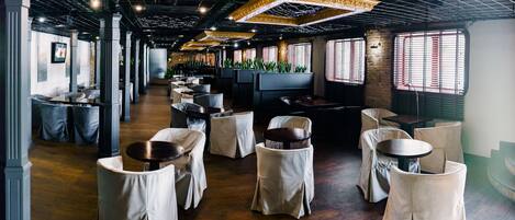 A spacious restaurant with high ceilings, exposed brick walls, and a long counter with tables and chairs.