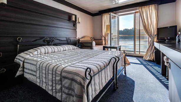 A hotel room with a bed, a desk, a television, and a view of the water. - Hotel Bakkara (Kyiv)