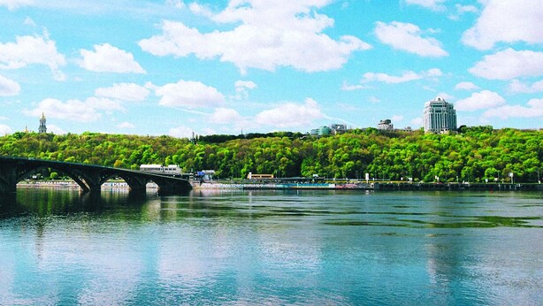 A stone bridge over a river with a forested hill in the background. - Hotel Bakkara (Kyiv)