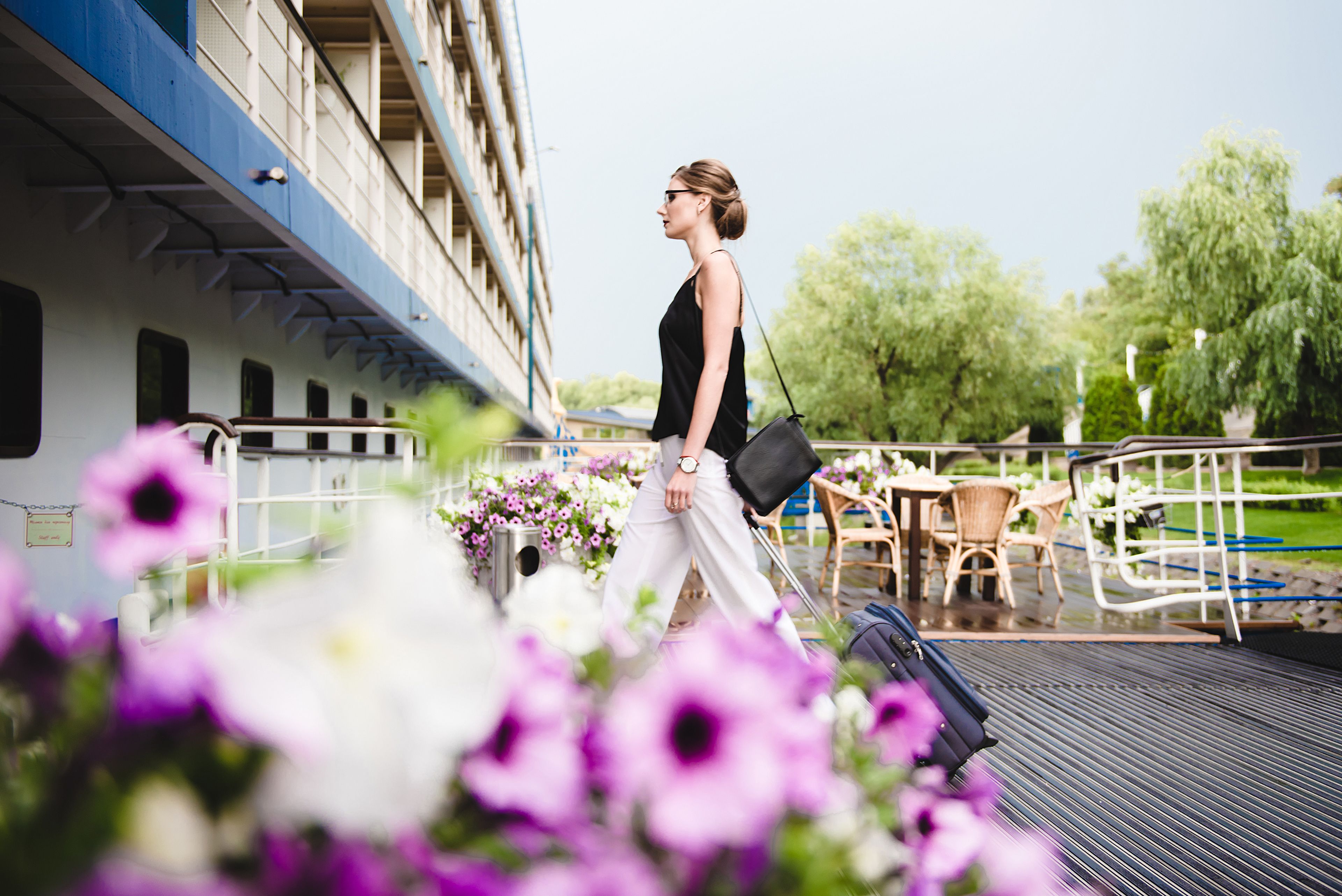 A woman walking on a deck with a railing, overlooking a body of water and greenery.