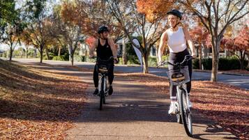 Dos personas andan en bicicleta por un camino pavimentado bordeado de árboles con follaje otoñal.