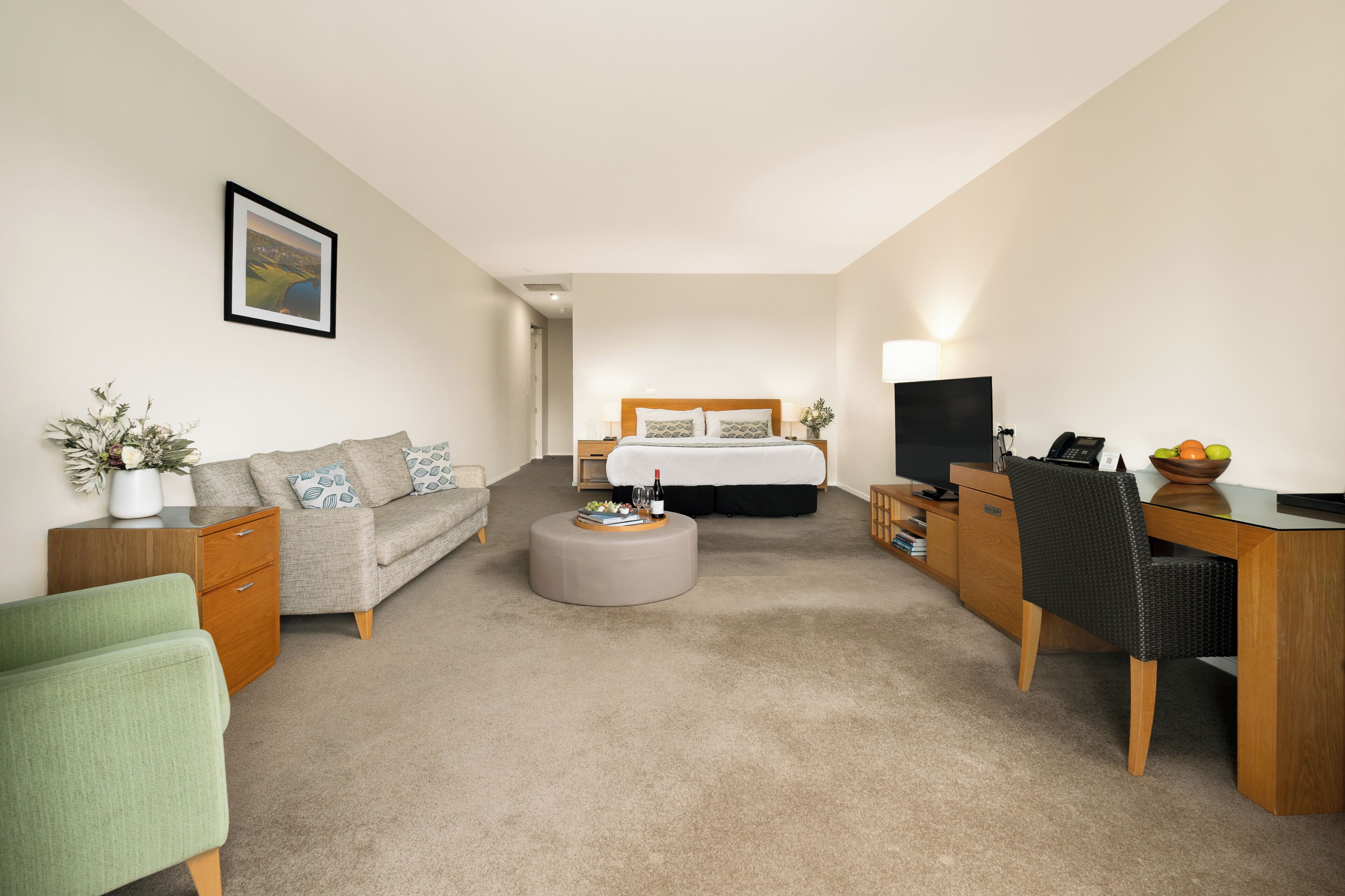 Una habitación de hotel con cama, escritorio, televisor, sofá y una pequeña mesa de centro.