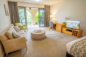 A modern hotel room with a sofa, ottoman, desk, and TV.