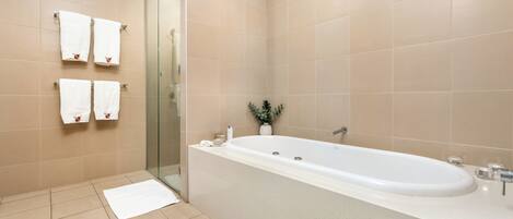 Une salle de bain moderne avec une grande baignoire, une douche en verre et plusieurs serviettes blanches ornées d’un logo.