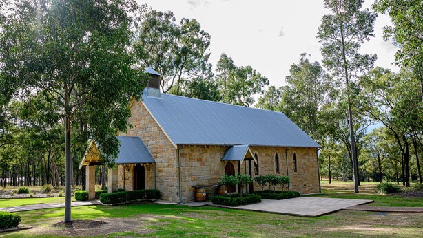 A stone building with a blue roof, surrounded by trees and a well-maintained lawn. - Chateau Elan At The Vintage (Pokolbin)