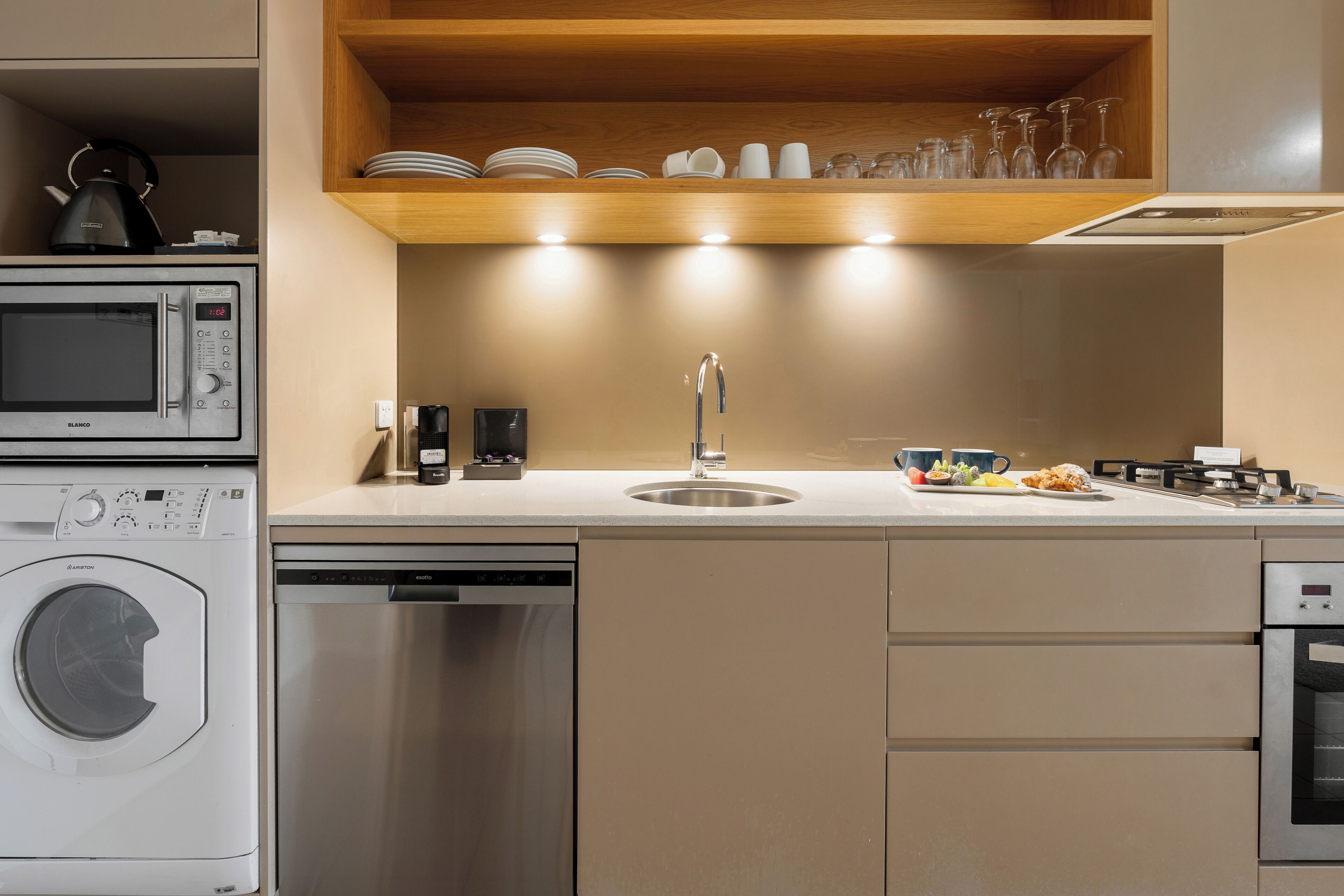 A modern kitchen with a built-in dishwasher, a microwave, a coffee machine, and a sink with a stainless steel faucet.