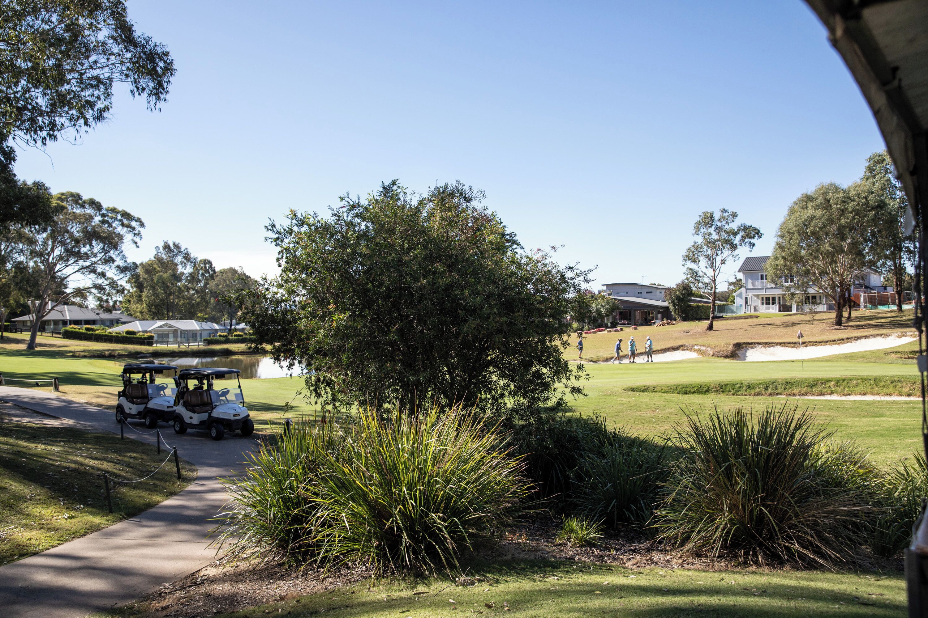 A golf course with a walking path, a golf cart, and residential buildings in the background.
