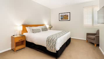 A bedroom with a bed, bedside table, lamp, chair, and a framed picture on the wall.