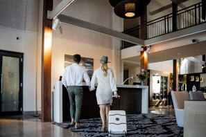 A couple holding hands in a hotel lobby with a reception desk, a patterned rug, and a staircase in the background. - Chateau Elan At The Vintage (Pokolbin)
