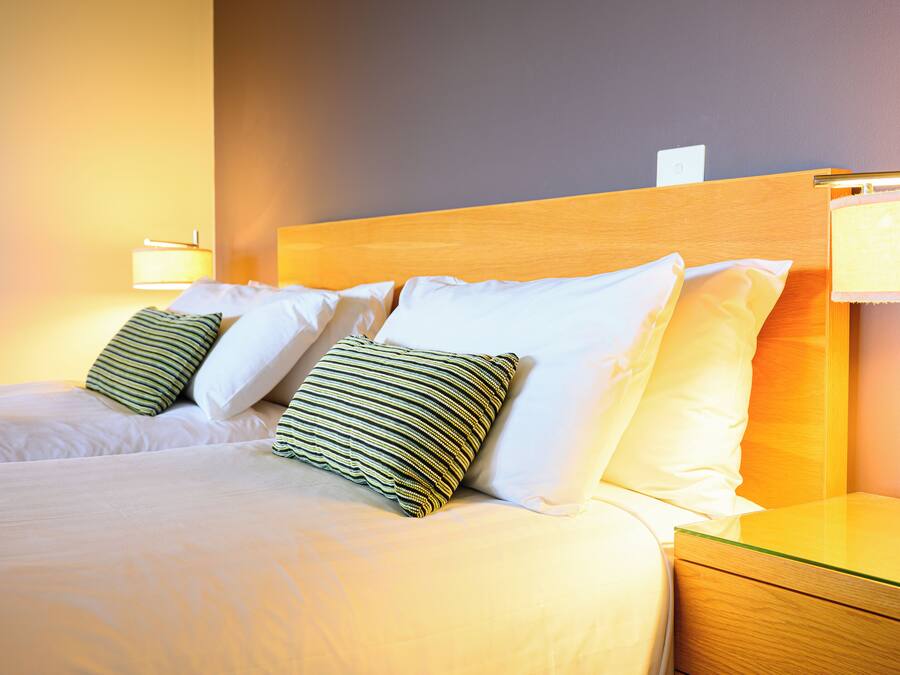 A neatly made bed with white and striped pillows, a wooden headboard, and a bedside table with a lamp.