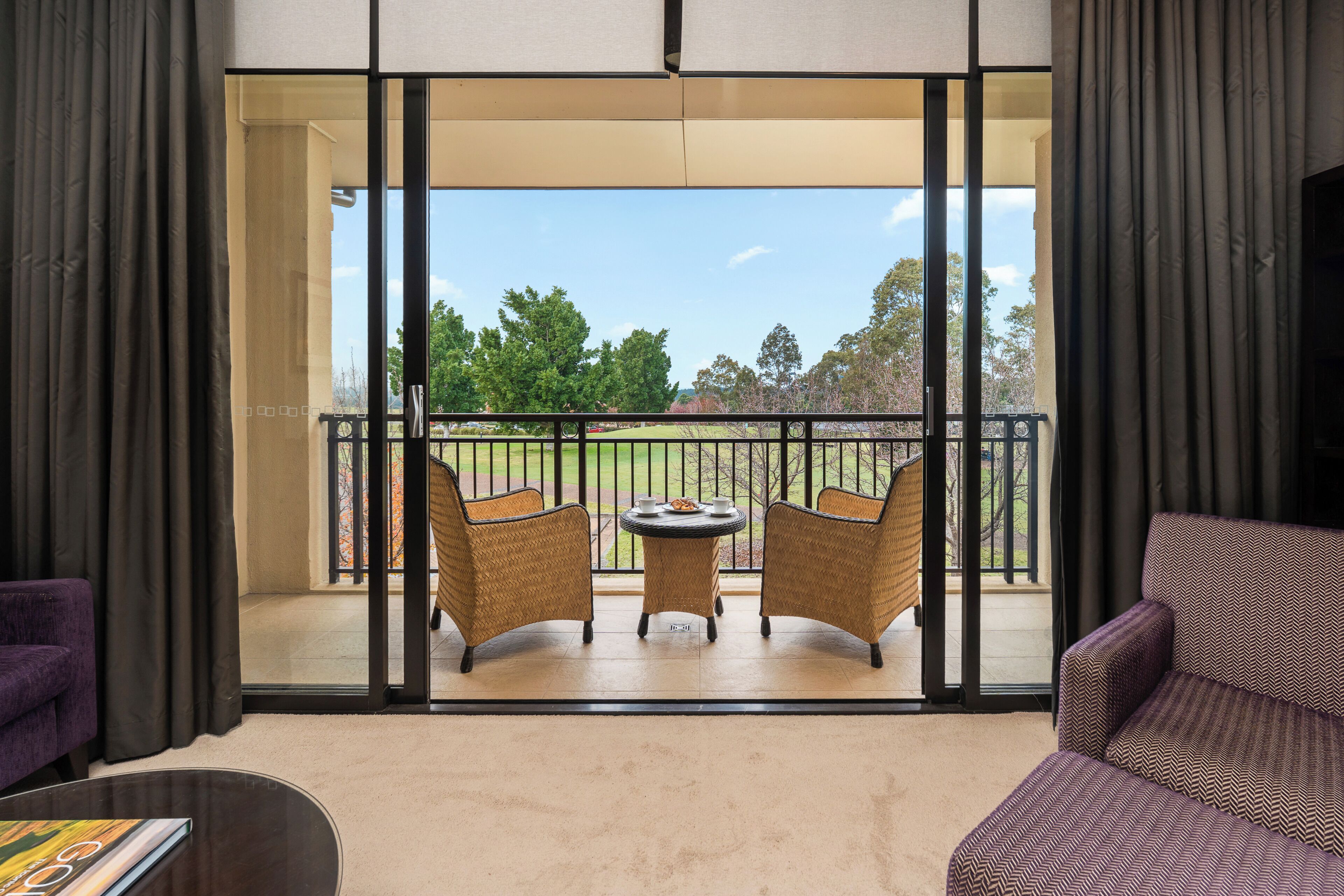 A room with a balcony, two wicker chairs, a small table, and a purple sofa.