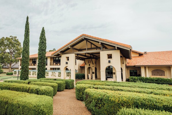 A building with a covered patio, a garden with neatly trimmed hedges, and tall trees. - Chateau Elan At The Vintage (Pokolbin)