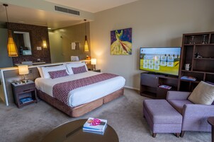 Una habitación de hotel con una cama grande, televisión, estantería y zona de estar.